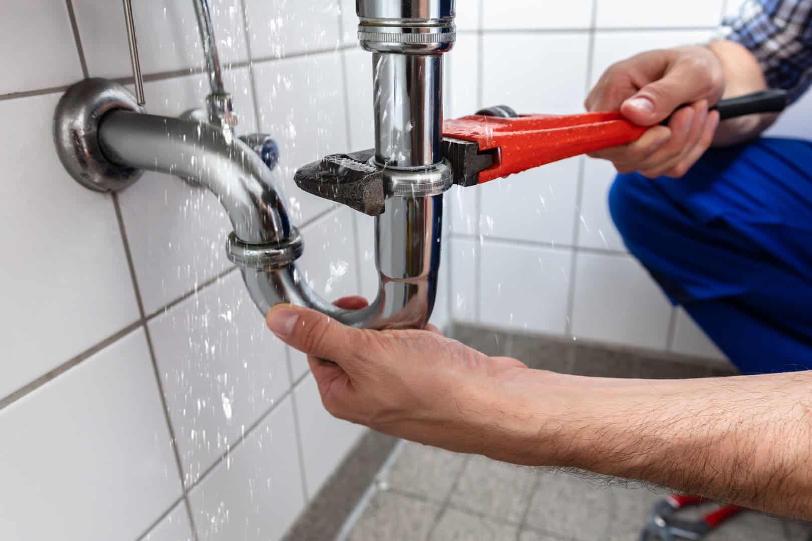 Plumber repairing a leaking waste pipe beneath a sink