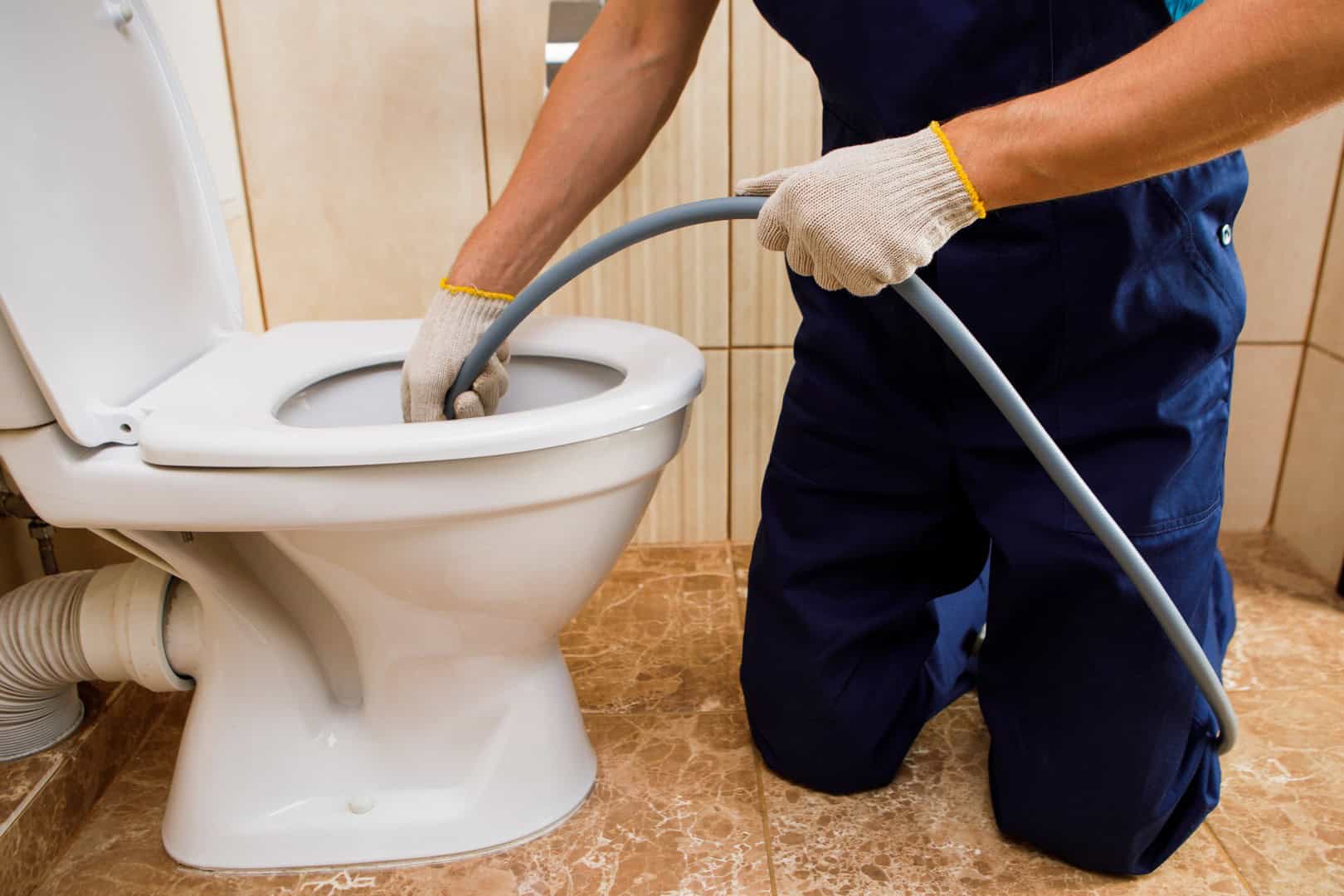 Drainage engineer using a jetting hose to clear a toilet